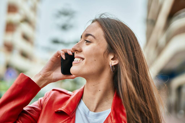 Νεαρή Ισπανίδα γυναίκα χαμογελά ευτυχισμένη μιλώντας στο smartphone της πόλης. - Φωτογραφία, εικόνα