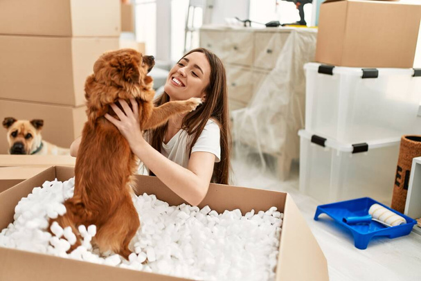 Young hispanic woman holding dog from package sitting on floor at new home - Фото, изображение