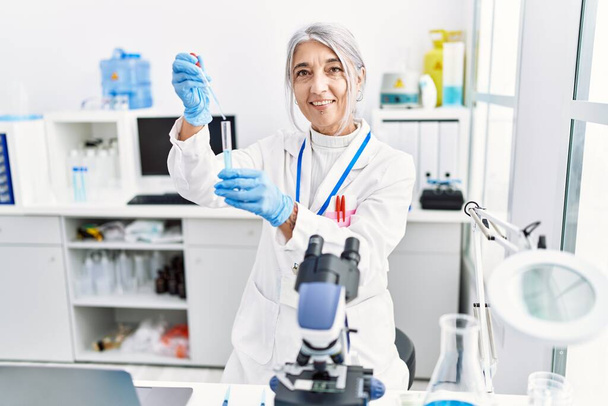 Kobieta w średnim wieku w mundurze naukowca, używająca pipety w laboratorium. - Zdjęcie, obraz