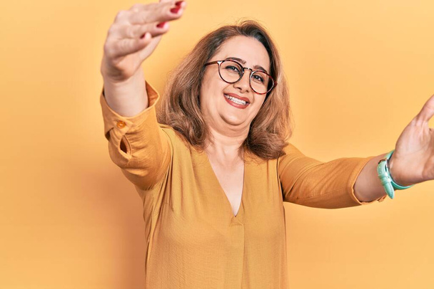 Middle age caucasian woman wearing casual clothes and glasses looking at the camera smiling with open arms for hug. cheerful expression embracing happiness.  - Fotografie, Obrázek