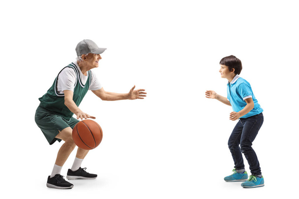 Full length profile shot of a senior and a child playing basketball isolated on white background - Foto, imagen