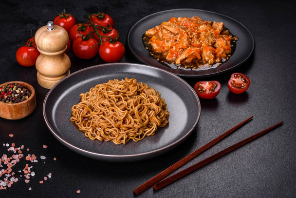 Teller mit gebratenen Nudeln und Gemüse mit scharfer Hühnersoße auf Restauranttisch, chinesische Küche - Foto, Bild