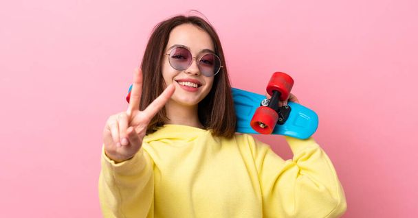 Young Ukrainian woman isolated on pink background with a skate doing victory gesture - Foto, imagen