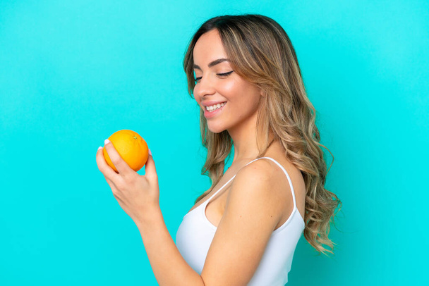 Fiatal fehér nő elszigetelt kék háttér kezében egy narancs - Fotó, kép
