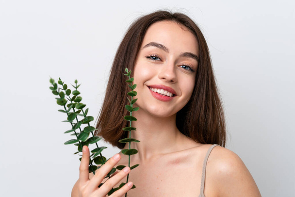 Young Ukrainian woman isolated on white background holding a eucalyptus branch while smiling. Close up portrait - Foto, Imagen