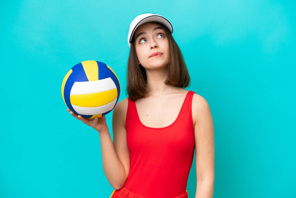 Young Ukrainian woman playing volleyball on a beach isolated on blue background and looking up - Фото, зображення