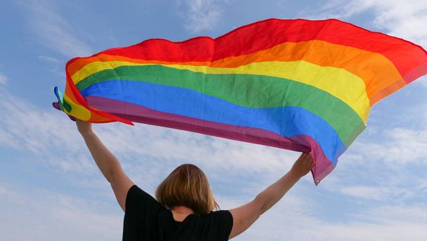 Woman lesbian holding LGBT flag on sky background - Фото, изображение