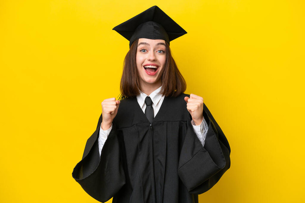Young university graduate Ukrainian woman isolated on yellow background celebrating a victory in winner position - Photo, image