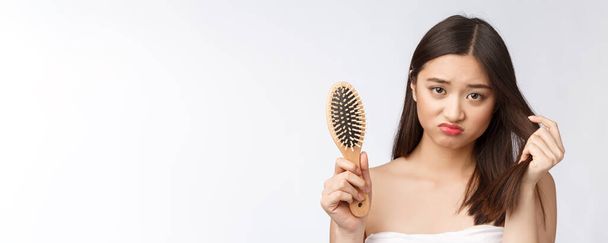 Molesto estresado joven mujer asiática sosteniendo el cabello seco dañado en las manos sobre fondo aislado blanco
. - Foto, Imagen