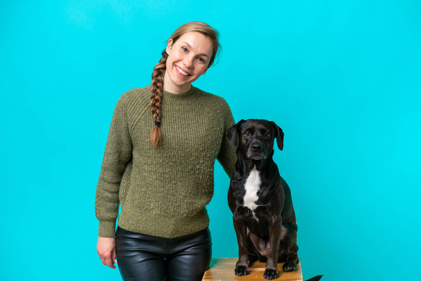 Nuori valkoihoinen nainen koiransa kanssa eristetty sinisellä taustalla hymyillen paljon - Valokuva, kuva