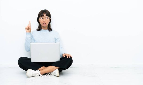 Young mixed race woman sitting on the floor with laptop isolated on white background intending to realizes the solution while lifting a finger up - 写真・画像