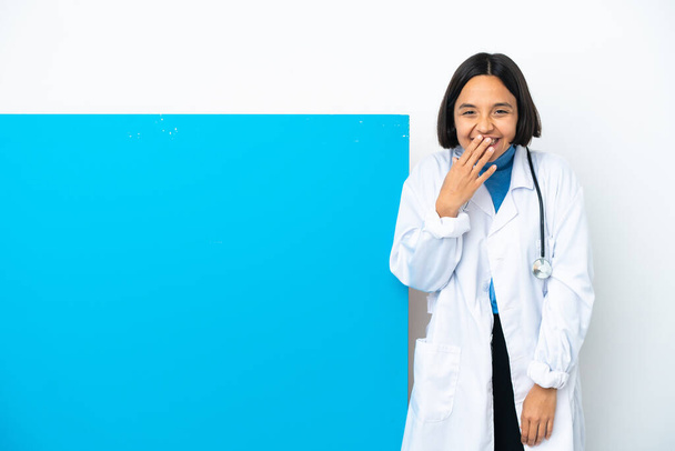 Mladý smíšený závod lékař žena s velkým štítkem izolované na bílém pozadí šťastný a usmívající se zakrývající ústa s rukou - Fotografie, Obrázek