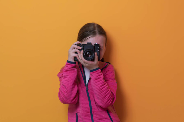 Little girl photographer isolated on yellow background smiling taking photos with a retro vintage camera.  - 写真・画像