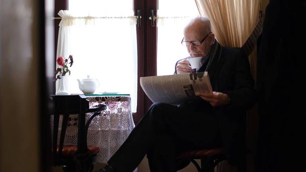 Šedovlasý dědeček sedí v kavárně a pije čaj, čte noviny.. - Fotografie, Obrázek