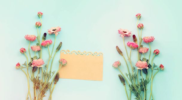 Top view image of pink flowers composition and empty note over blue pastel background - Photo, Image