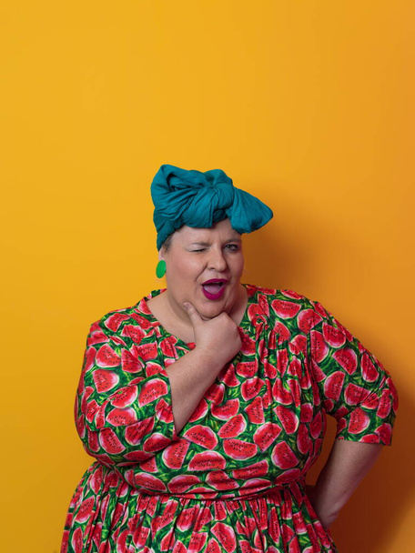 Funny plus size sexy model woman with trendy makeup, fashionable overweight blonde in colorful dress posing at the yellow background in studio. - 写真・画像