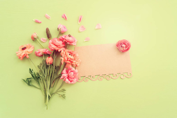 Top view image of pink flowers composition and empty note over green wooden background - Foto, imagen