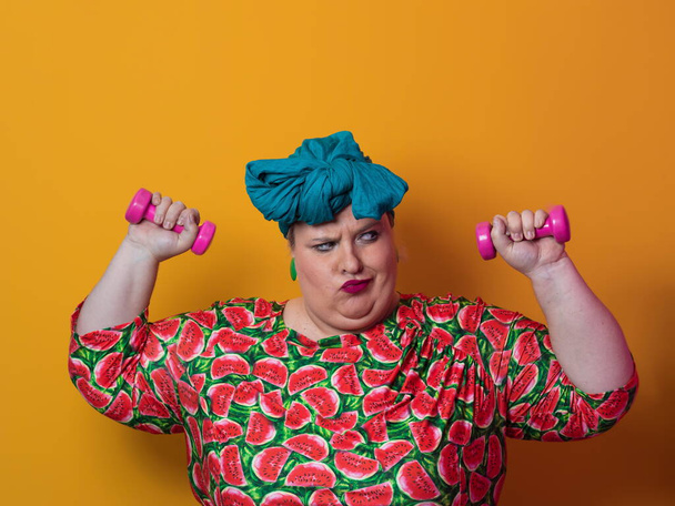 Fat woman dieting, fitness and health at home.Big woman and sport. Healthy, fitness and sports concept. Plus size young woman doing exercise with dumbbells on yellow background. - Zdjęcie, obraz