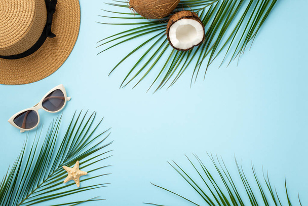 Letní koncept. Horní pohled fotografie klobouku kokosové ořechy stylové sluneční brýle hvězdice a palmové listy na izolovaném pastelově modrém pozadí s copyspace - Fotografie, Obrázek