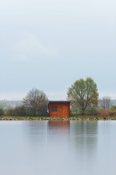 Wooden cabin, building on pond shore in rain moody weather. Long exposure, Czech landscape - Foto, imagen