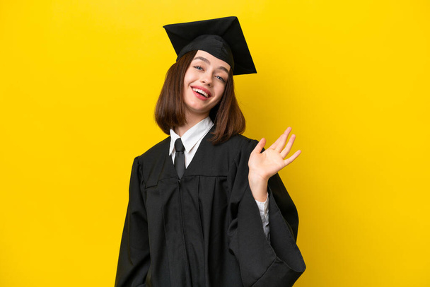 Young university graduate Ukrainian woman isolated on yellow background saluting with hand with happy expression - Valokuva, kuva