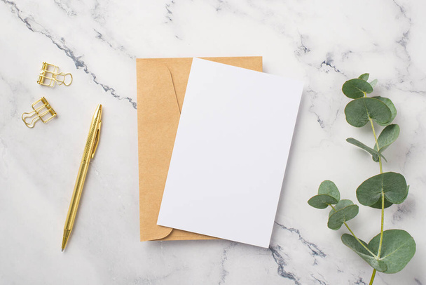 Верхний вид фото бумаги лист бумаги конверт золотой ручкой скрепки и эвкалиптовой ветви на белом мраморном фоне с пустым пространством - Фото, изображение