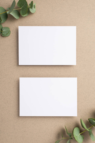 Business concept. Top view vertical photo of two paper cards and eucalyptus on beige background with empty space - Foto, afbeelding