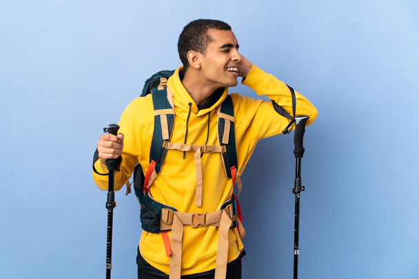African American man with backpack and trekking poles over isolated background listening to something by putting hand on the ear - Valokuva, kuva