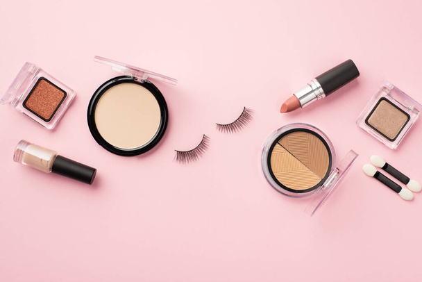 Makeup concept. Top view photo of false eyelashes lipstick compact powder contouring palette eyeshadow brushes and nail polish on pastel pink background - Photo, Image