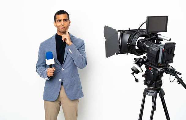 Reportero afroamericano sosteniendo un micrófono y reportando noticias sobre fondo blanco aislado y pensando - Foto, imagen