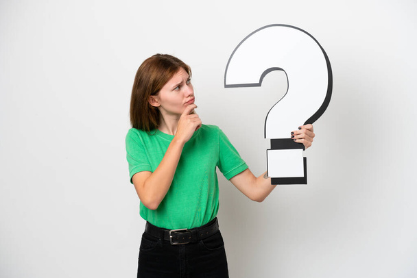 Young English woman isolated on white background holding a question mark icon and having doubts - 写真・画像