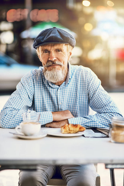 Emerytura dobrze na tobie wygląda. Portret szczęśliwego starszego mężczyzny pijącego kawę w kawiarni przy chodniku. - Zdjęcie, obraz