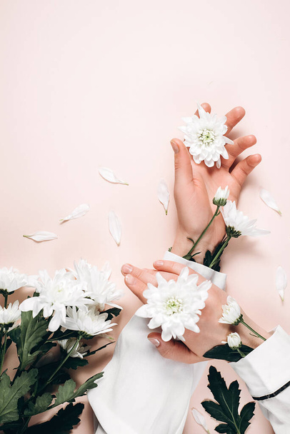 Creative image of beautiful groomed woman's hands with white flowers with copy space on pink color background wall in minimalist style. Concept template feminine blog, social media, beauty concept - Фото, изображение