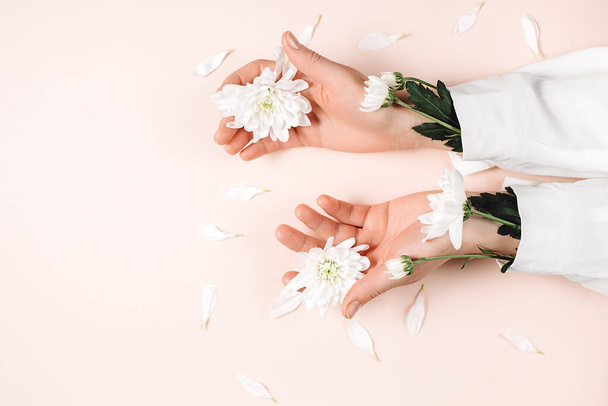Beauty female hands with fresh beautiful flowers on pastel pink color background wall in studio with copy space for promotion content. Natural cosmetic for hand skin care. Flat lay, fashion concept - Fotó, kép