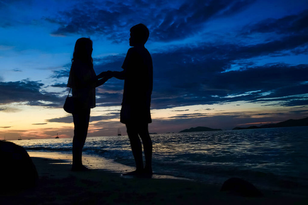 Deniz kenarındaki siluette romantik bir çift gün batımının, tatil manzarasının tadını çıkarıyor. - Fotoğraf, Görsel