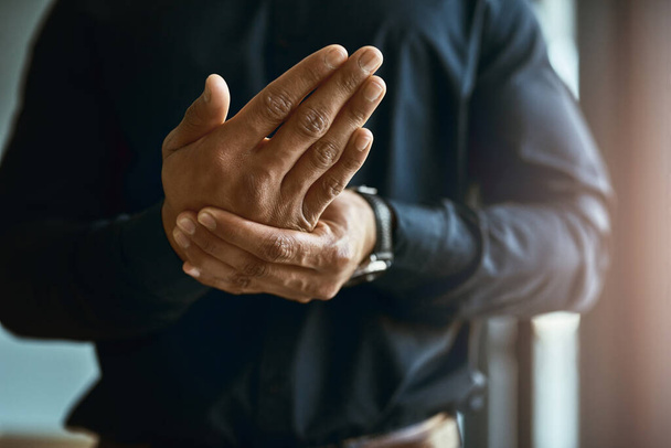Feeling numbness and pain in his hands. Closeup shot of an unidentifiable businessman suffering with pain in his hands. - Photo, image