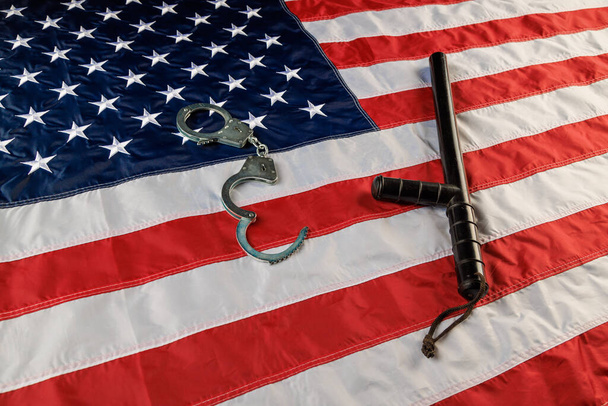 Срібні металеві наручники і поліцейські нічні панчохи над прапором США на плоскій поверхні. - Фото, зображення