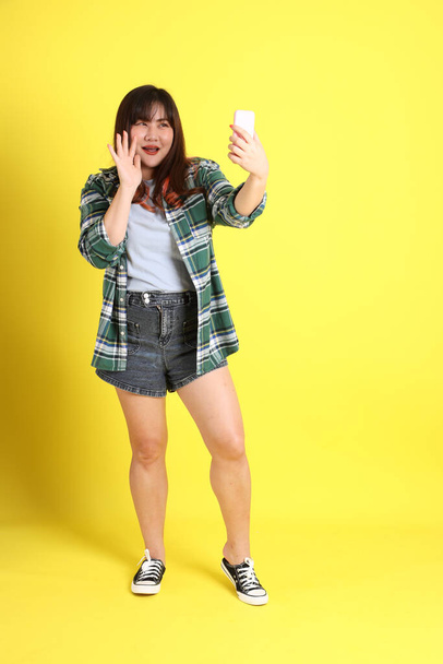 The chubby Asian woman standing on the yellow background with the casual clothes. - Photo, image