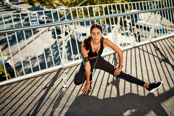 Пора поднять уровень фитнеса. Снимок спортивной молодой женщины, растянувшейся перед пробежкой по городу. - Фото, изображение