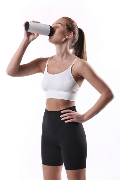 Mujer fitness bebiendo agua de una botella. Hermosa chica atlética en el fondo blanco - Foto, imagen