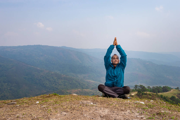 man mediteren op heuvel top met mistige berg woede achtergrond van platte hoek afbeelding wordt genomen op nongjrong meghalaya india. - Foto, afbeelding