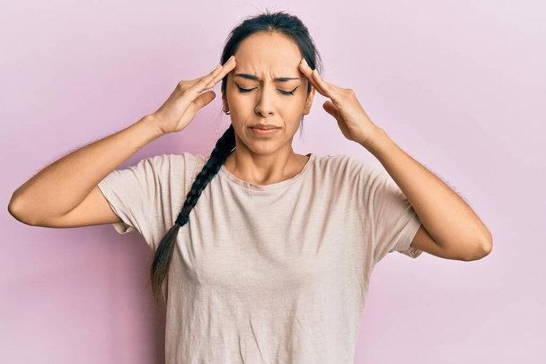Jong Latijns-Amerikaans meisje draagt casual wit t-shirt met de hand op het hoofd, hoofdpijn vanwege stress. lijden aan migraine.  - Foto, afbeelding