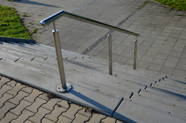 betonnen trap met roestvrijstalen gepolijste buisrailing. kasseien kasseien beton. vastgeschroefd aan de grond, detail - Foto, afbeelding