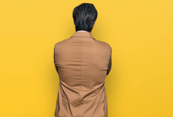 Jovem hispânico vestindo roupas de negócios olhando para trás com os braços cruzados  - Foto, Imagem