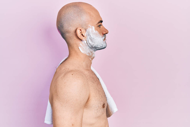 Young bald man shirtless shaving beard with foam looking to side, relax profile pose with natural face with confident smile.  - Photo, image