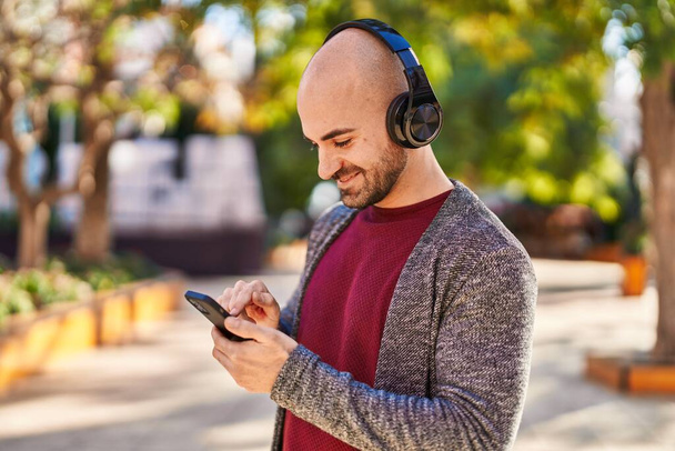 Νεαρός άνδρας χαμογελά σίγουρος ακούγοντας μουσική στο πάρκο - Φωτογραφία, εικόνα