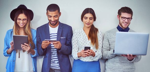 Спіймати в соціальних мережах, поки ви чекаєте. Студійний знімок групи молодих бізнесменів, які використовують бездротові технології, стоячи в черзі на сірому фоні
. - Фото, зображення
