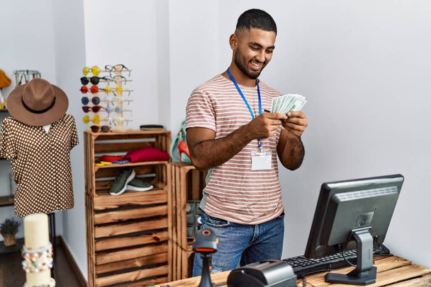 Young arab man holding dollars working at clothing store - Foto, imagen