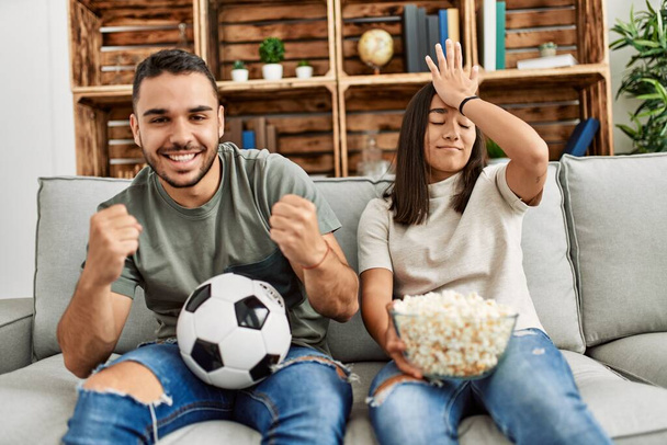 Νεαρό ζευγάρι Λατίνων βλέποντας ποδόσφαιρο αγώνα τρώει καλαμπόκι στο σπίτι. - Φωτογραφία, εικόνα