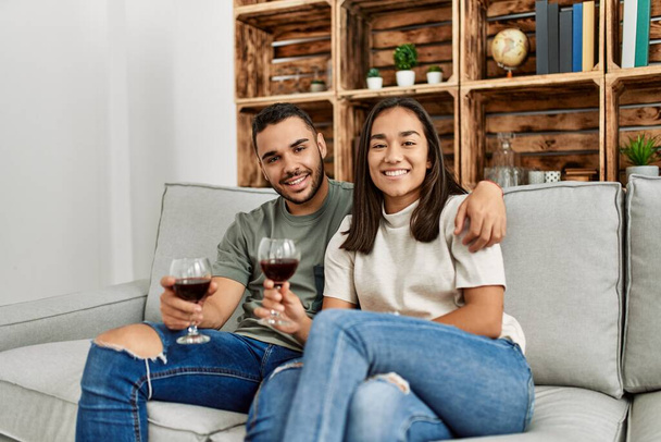 Jeune couple latin souriant heureux toasting avec verre de vin rouge à la maison. - Photo, image